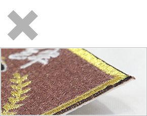 ワッペンのロック加工:周囲にロックをかけず、熱で焼ききったカットのみの加工。固まった部分が鋭利になっており危険。